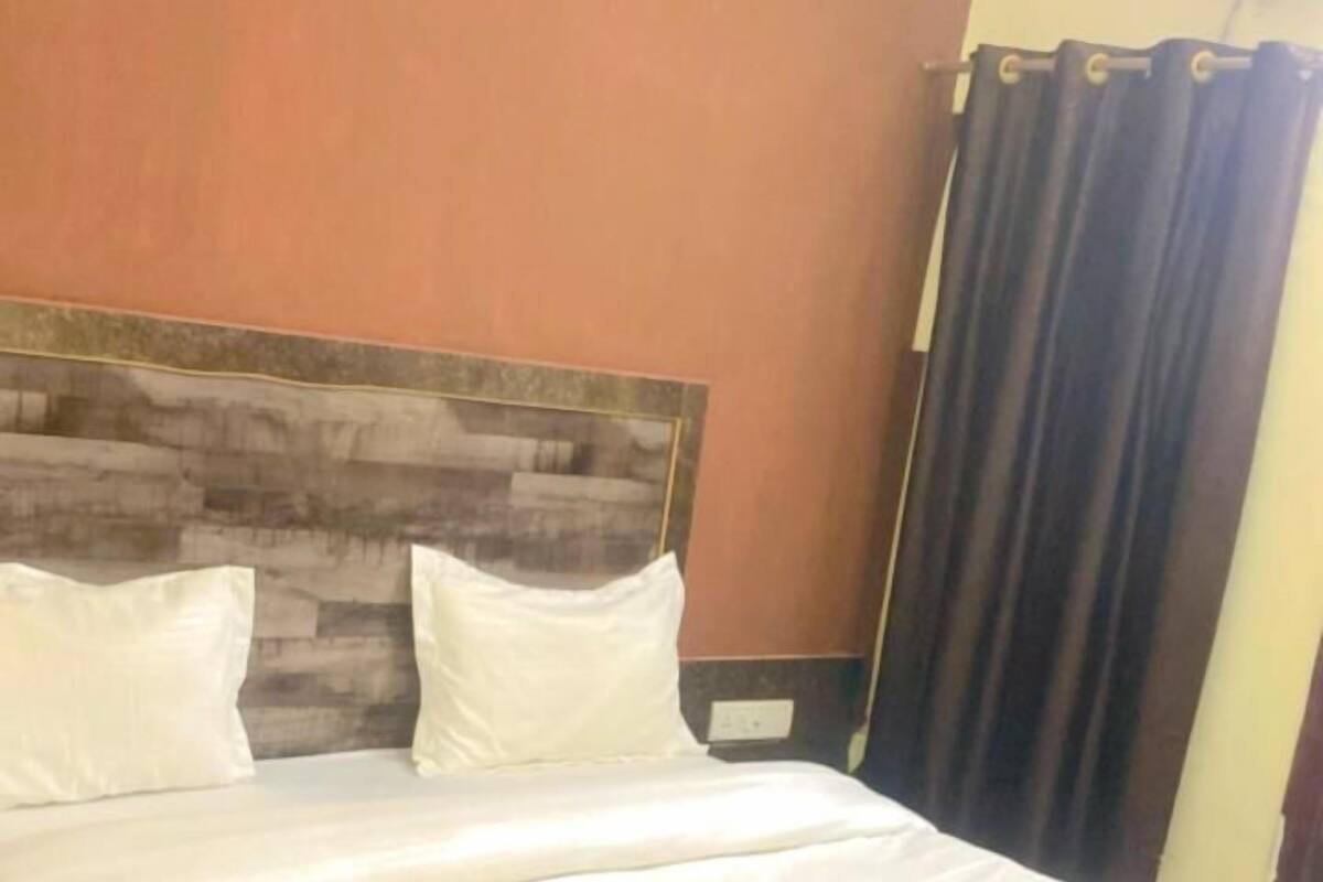 A bed with white linens, a wooden headboard, and a dark curtain.