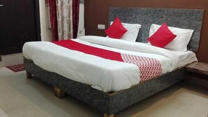 Un lit double avec une tête de lit grise et une literie blanche, des coussins rouges et un plaid rouge et blanc à motifs.