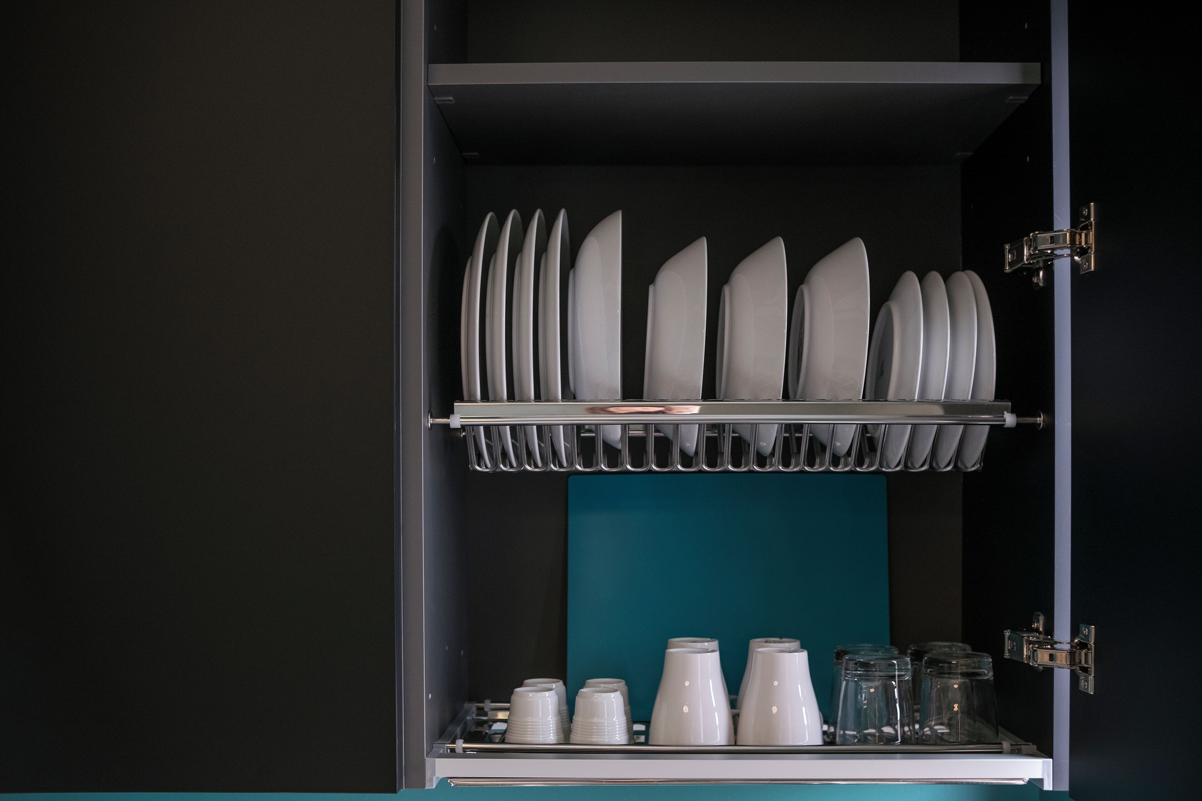 Un armario de cocina con platos y tazones blancos en la repisa superior y tazas y frascos de vidrio en la repisa inferior.