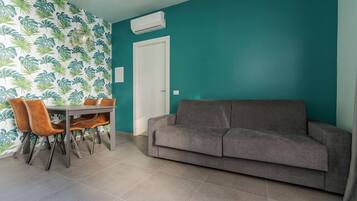 A living room with teal walls, a gray sofa, and a dining table with orange chairs.