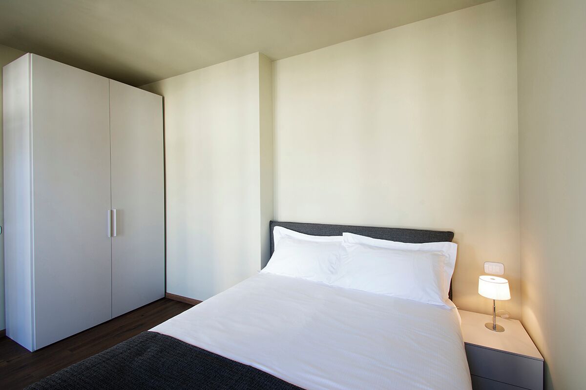 Une chambre d’hôtel avec un lit, une table de chevet avec une lampe et une armoire.