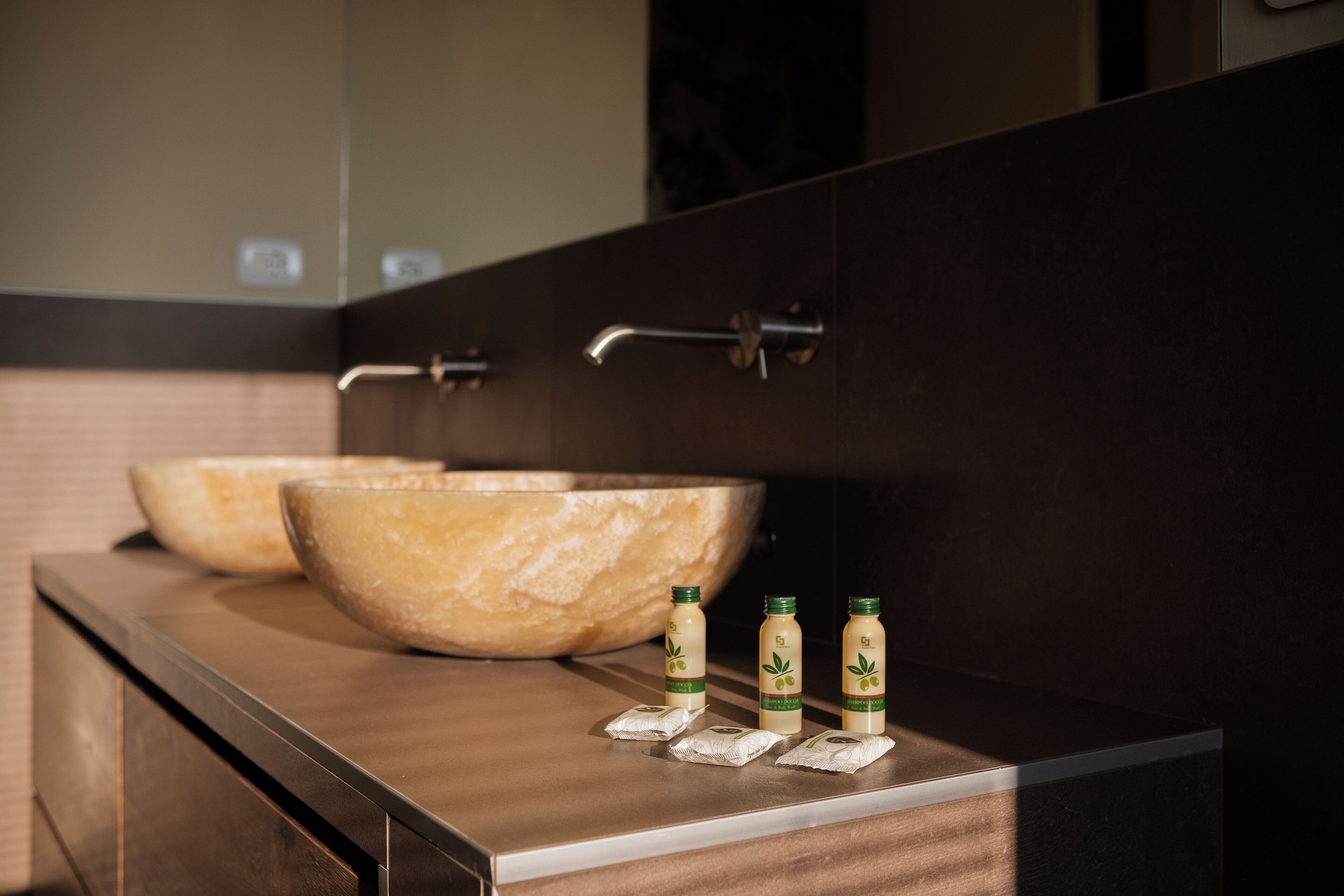 Une salle de bain avec deux grands lavabos en marbre et trois bouteilles de lotion posées sur le comptoir.