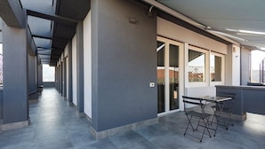 Un pasillo con una zona de estar techada al aire libre, una entrada con puerta de vidrio y vistas al exterior.