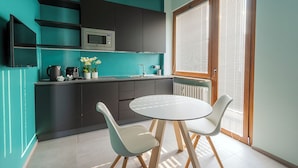 Una cocina moderna con armarios oscuros, un microondas y un lavamanos. Hay una mesa redonda con dos sillas y una pequeña planta en maceta sobre la encimera.
