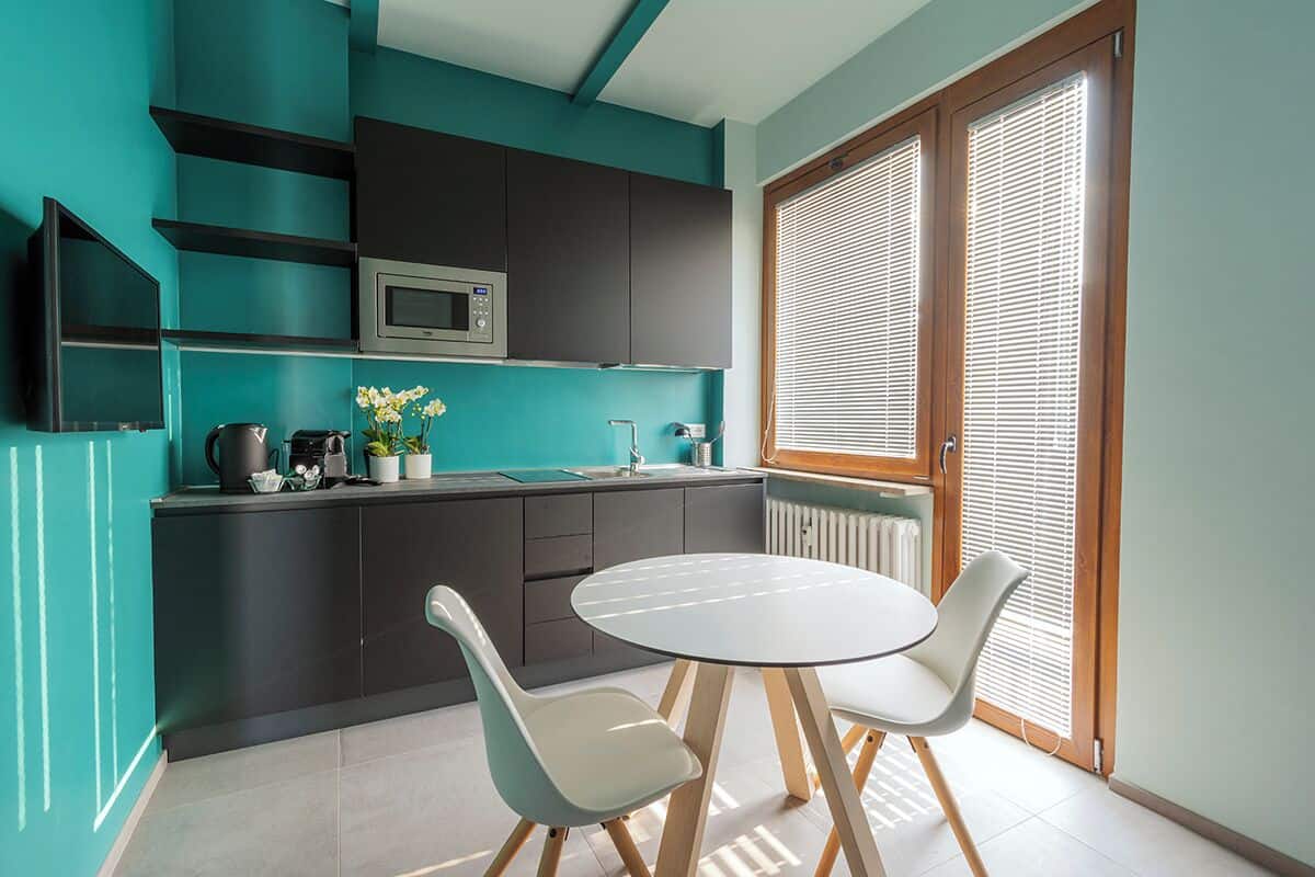 A modern kitchen with dark cabinets, a microwave, and a sink. There is a round table with two chairs and a small potted plant on the counter.
