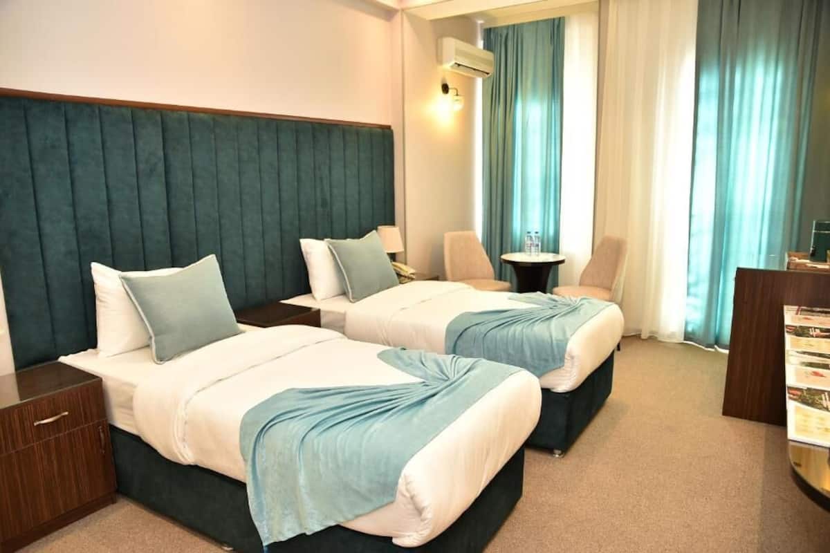 A hotel room with two beds, a desk, a chair, and a minibar.