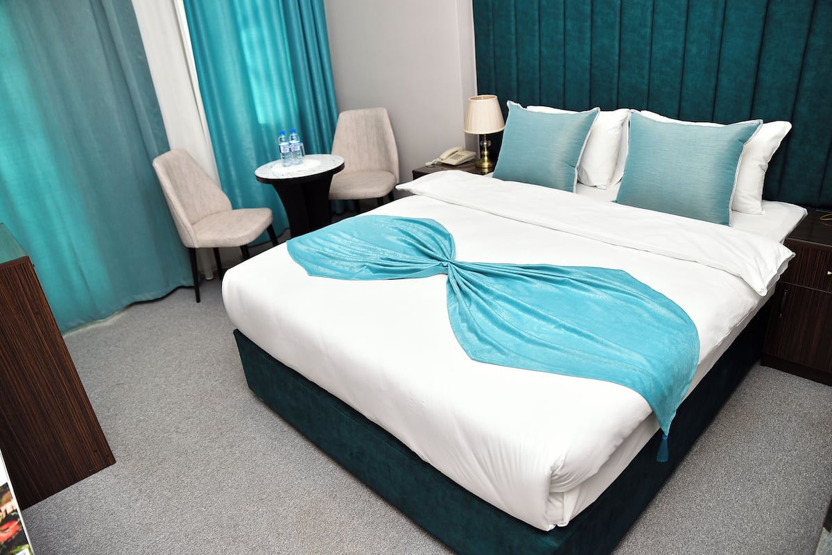 A hotel room with a bed, two chairs, a small table with water bottles, a lamp, and a telephone.