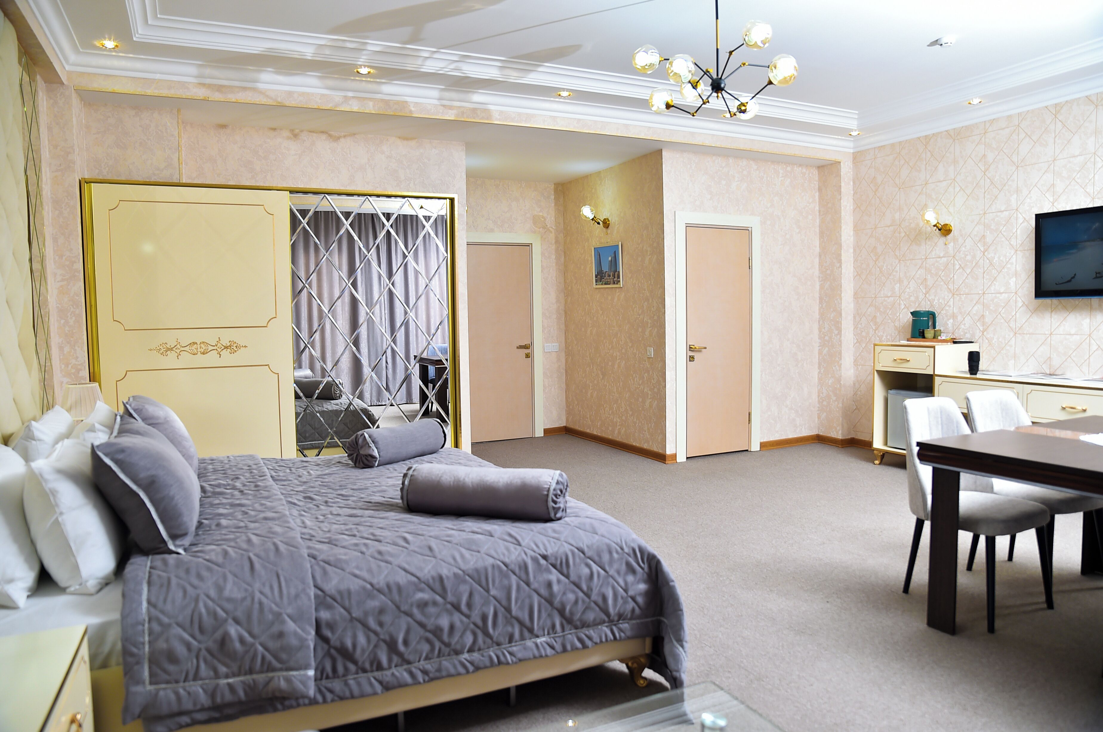 Camera d'albergo con un letto, un tavolo da pranzo e sedie. C'è una TV montata a parete e un lampadario.