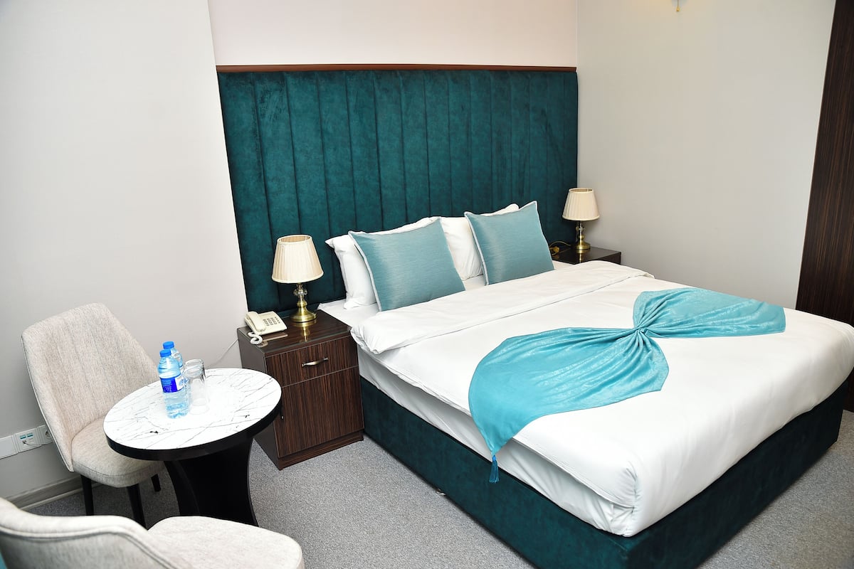 A hotel room with a bed, two bedside tables, a chair, and a small round table with a water bottle and a glass.