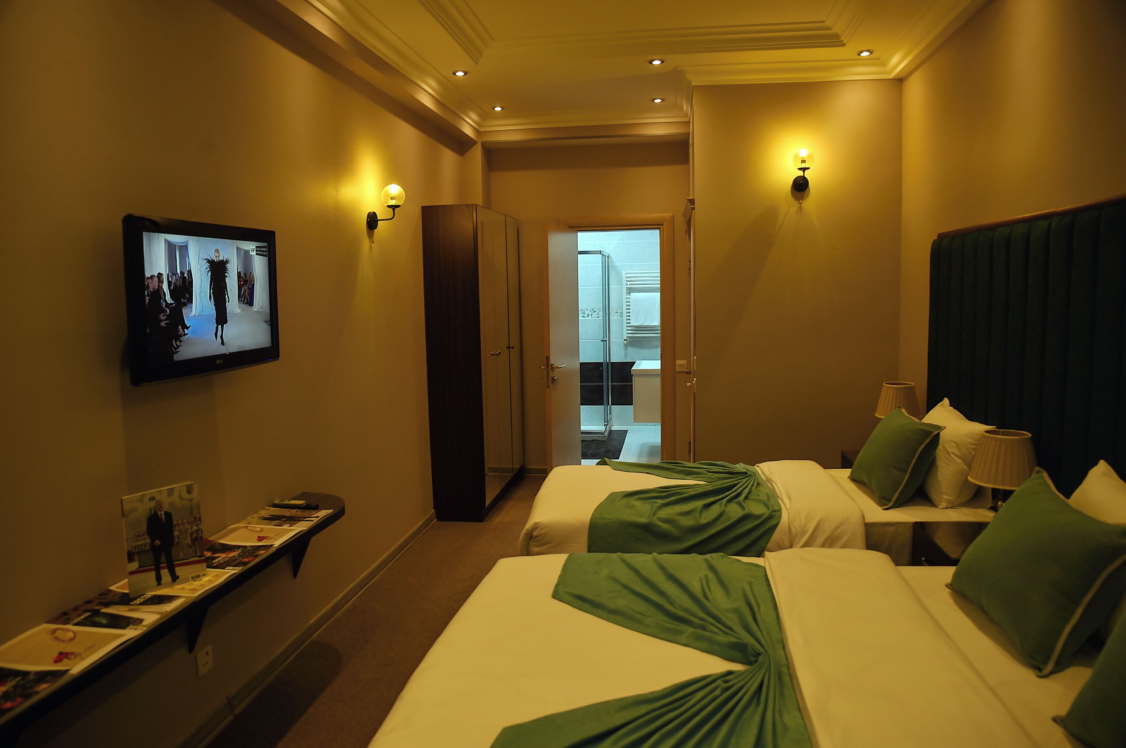 A hotel room with two beds, a television on the wall, and a hallway leading to a balcony.