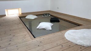 Ein kleiner, schräger Raum mit Holzboden, einem Drahtgitterrost und einem Dachfenster.