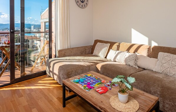 Ein modernes Wohnzimmer mit einem großen Fenster, einem Sofa, einem Couchtisch mit einem Gesellschaftsspiel und einer Topfpflanze.