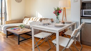 A modern living room with a sofa, dining table, chairs, a lamp, and a kitchen area with appliances.