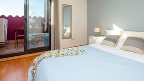A bedroom with a bed, a nightstand, a lamp, a mirror, and a view of the outside through a glass door.
