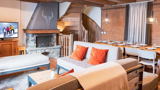 A cozy living room with a stone fireplace, wooden beams, and a dining area with a table set for four.