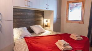 A bedroom with a wooden headboard, a red blanket, and towels on the bed.