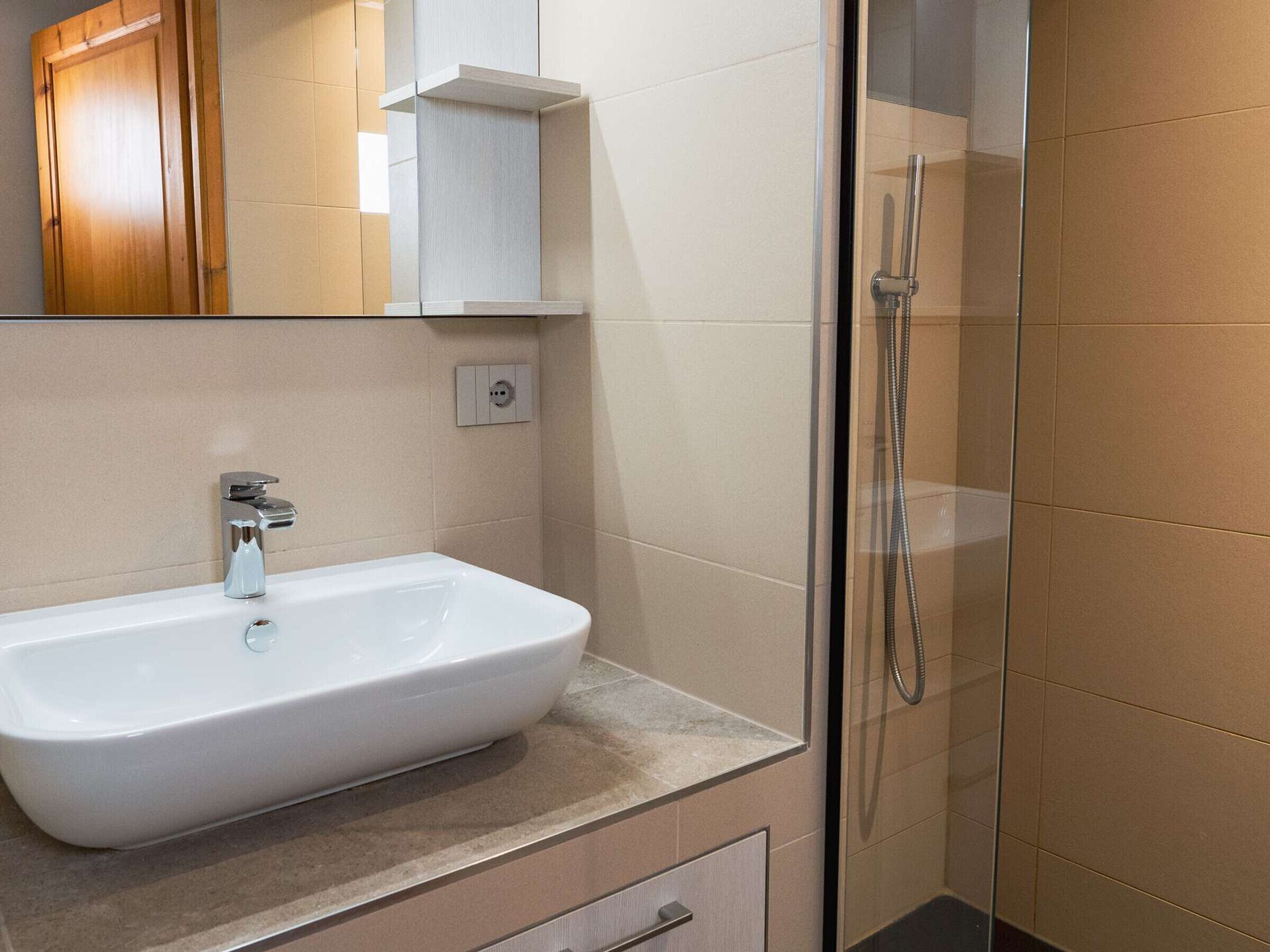 Une salle de bain avec un lavabo blanc, un miroir et une cabine de douche en verre.