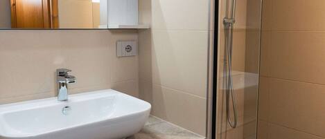 Une salle de bain avec un lavabo blanc, un miroir et une cabine de douche en verre.