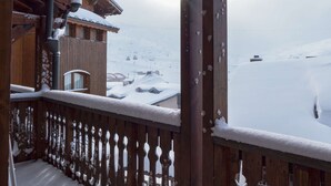 A wooden balcony with snow-covered railings and a view of a snow-covered mountain landscape.