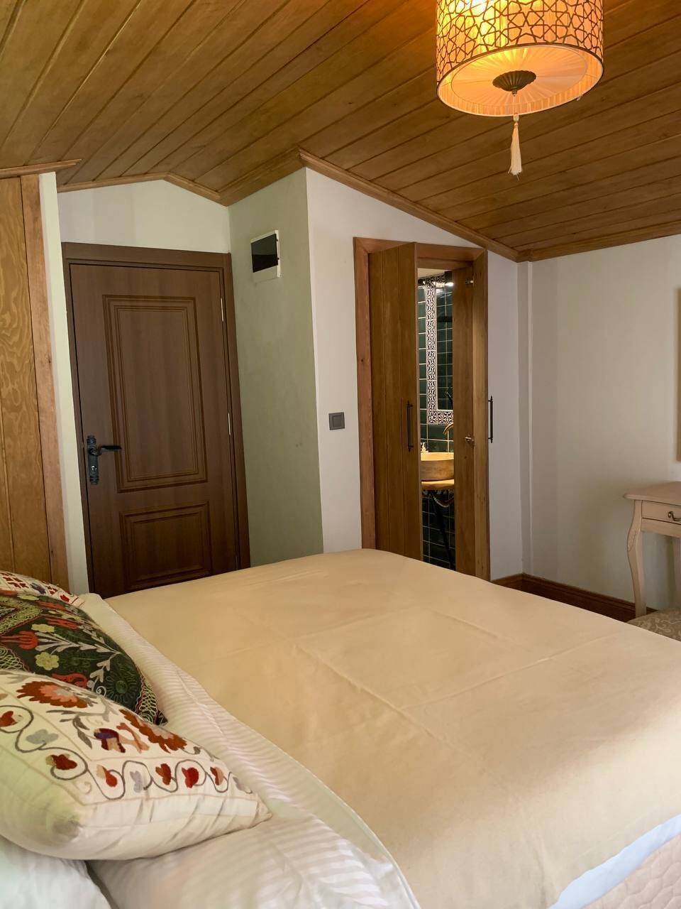 A bedroom with a bed, wooden ceiling, and a door leading to another room.