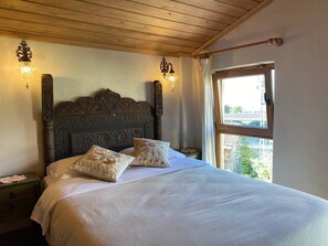 A bed with a wooden headboard, two wall sconces, and a window with curtains. - Sofia Konaklama (Istanbul)