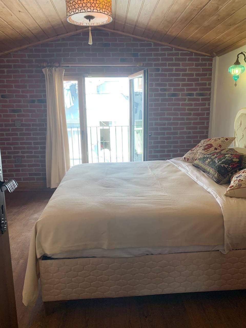 A bedroom with a large bed, a brick wall, a window, and a hanging light fixture.
