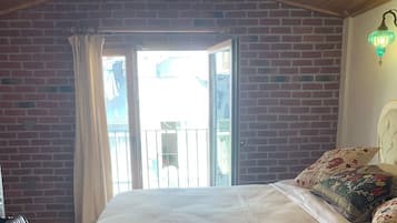 A bedroom with a large bed, a brick wall, a window, and a hanging light fixture.