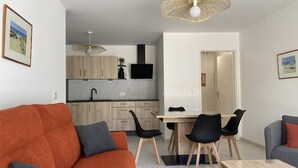 Ein modernes Wohnzimmer mit einer Couch, einem Esstisch mit Stühlen und einer Küche im Hintergrund.