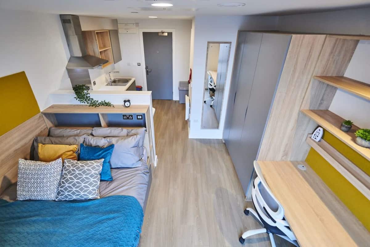 A compact, modern room with a bed, bedside table, and a small kitchenette.