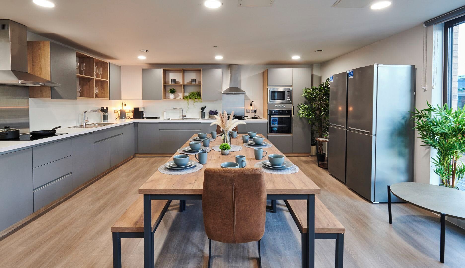 Una cocina moderna con armarios grises, una mesa de comedor de madera para seis personas y un refrigerador grande.