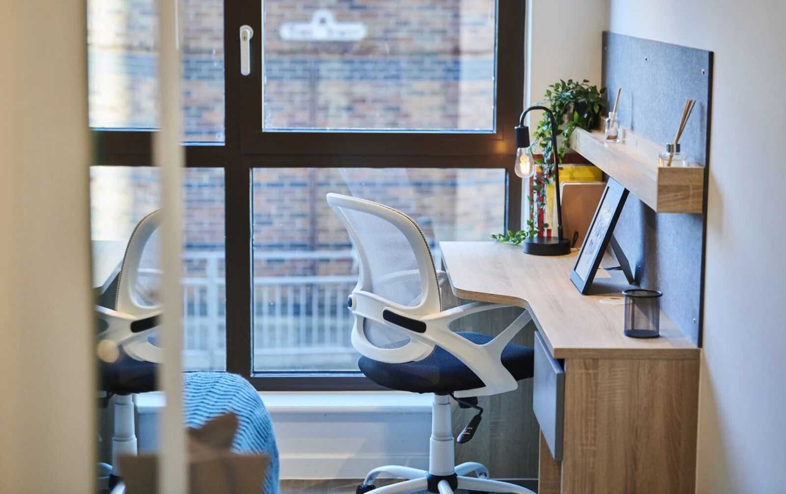 A modern office chair with a mesh backrest and a wooden desk with a small plant and a picture frame.