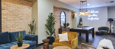 Una sala de estar moderna con un sofá azul, un sillón amarillo y una mesa de centro de madera. Hay una pared de ladrillo y un letrero de neón en la pared.