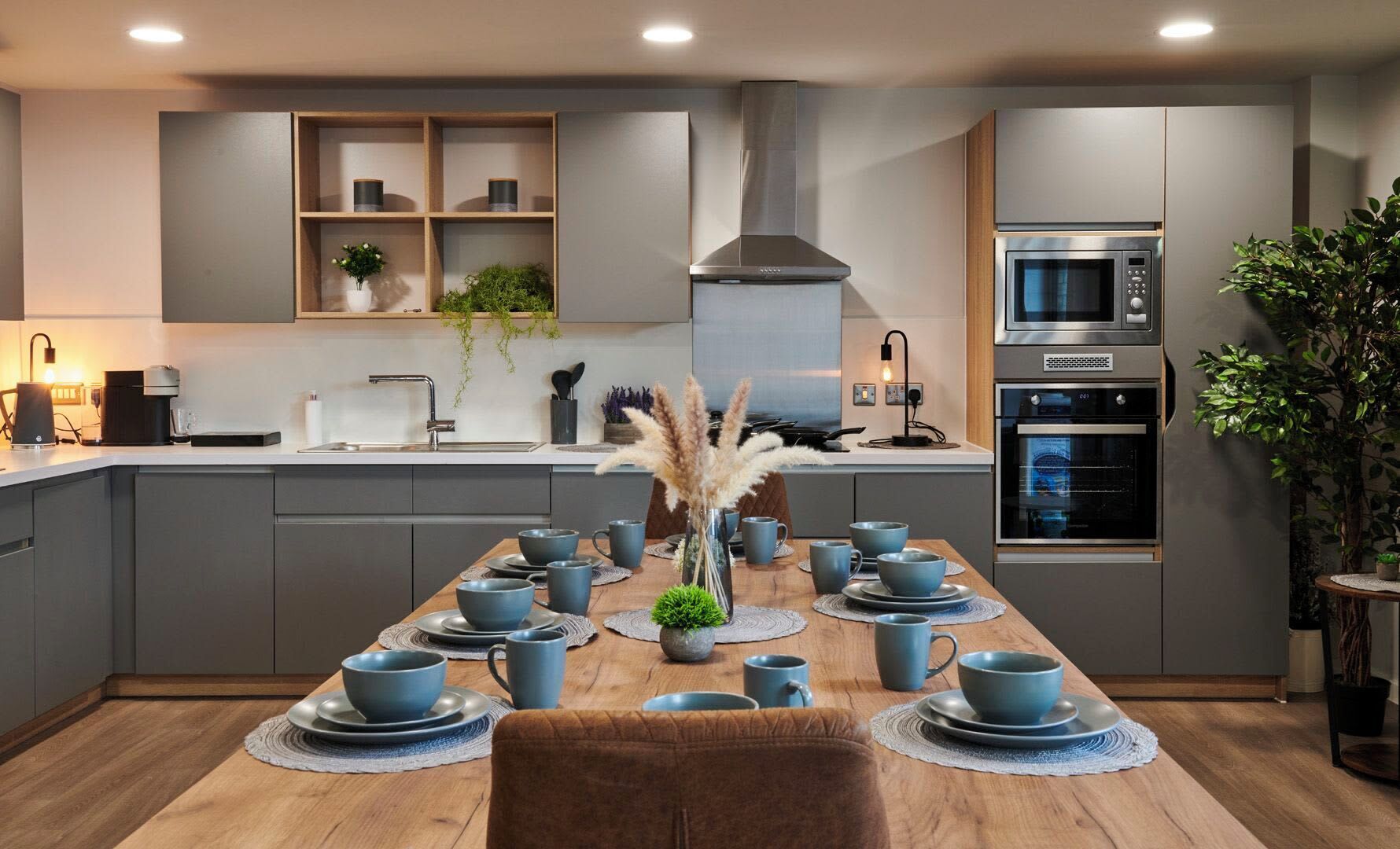 A modern kitchen with grey cabinetry, a central island with blue cups and saucers, and built-in appliances including a microwave and oven.