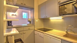 A compact kitchen with white cabinets, a built-in microwave, a sink, and a dishwasher. - 3-room apartment with southwest view and wifi in Morzine (Morzine)
