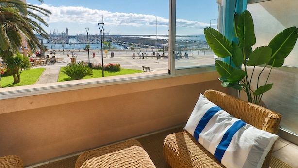 Un balcó amb vista al port esportiu, moble de vugada i una planta gran.
