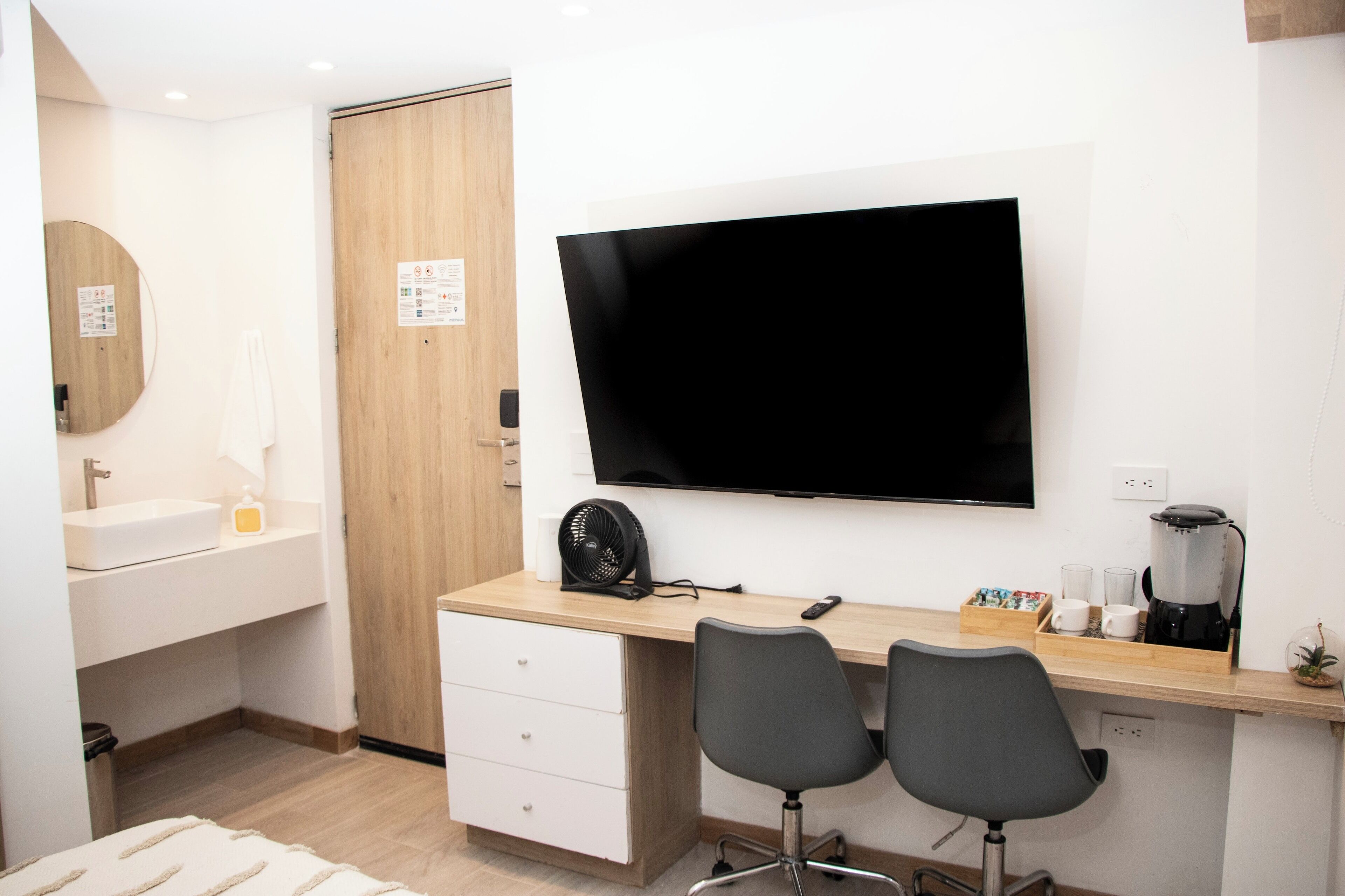 Une chambre d’hôtel moderne, dotée d’un bureau en bois, de deux chaises, d’un téléviseur à écran plat, d’une machine à café et d’une petite plante.