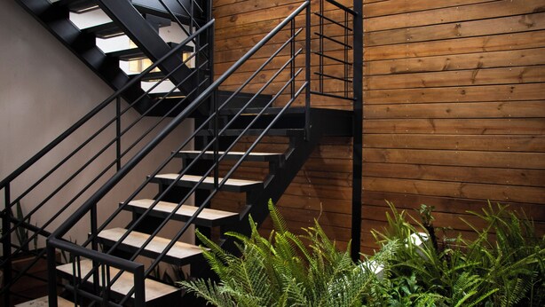 A staircase with black railings and wooden steps, leading to a wooden wall. - zenia (Medellín)