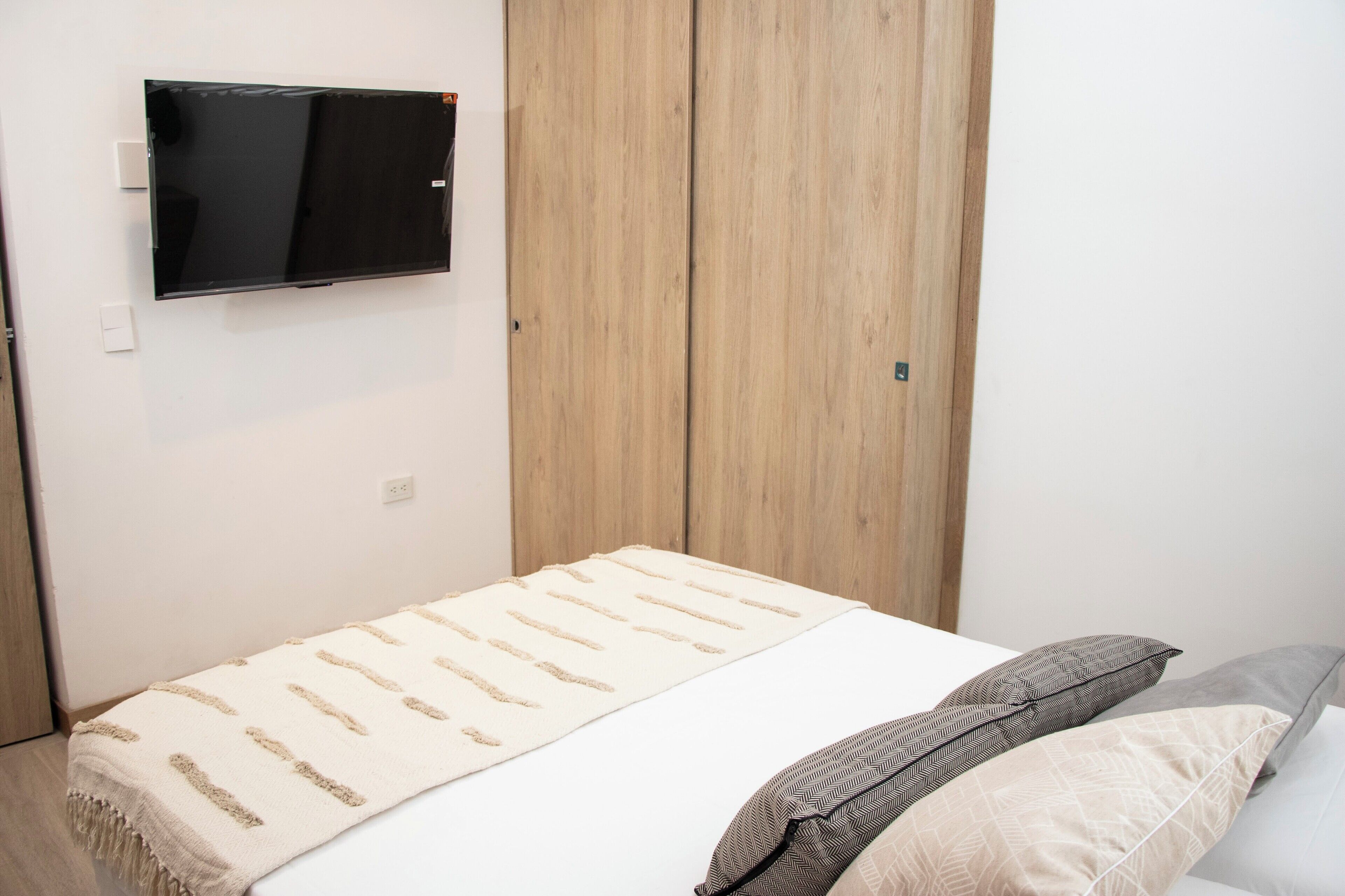 Un dormitorio con una cama, un televisor en la pared y armarios de madera.
