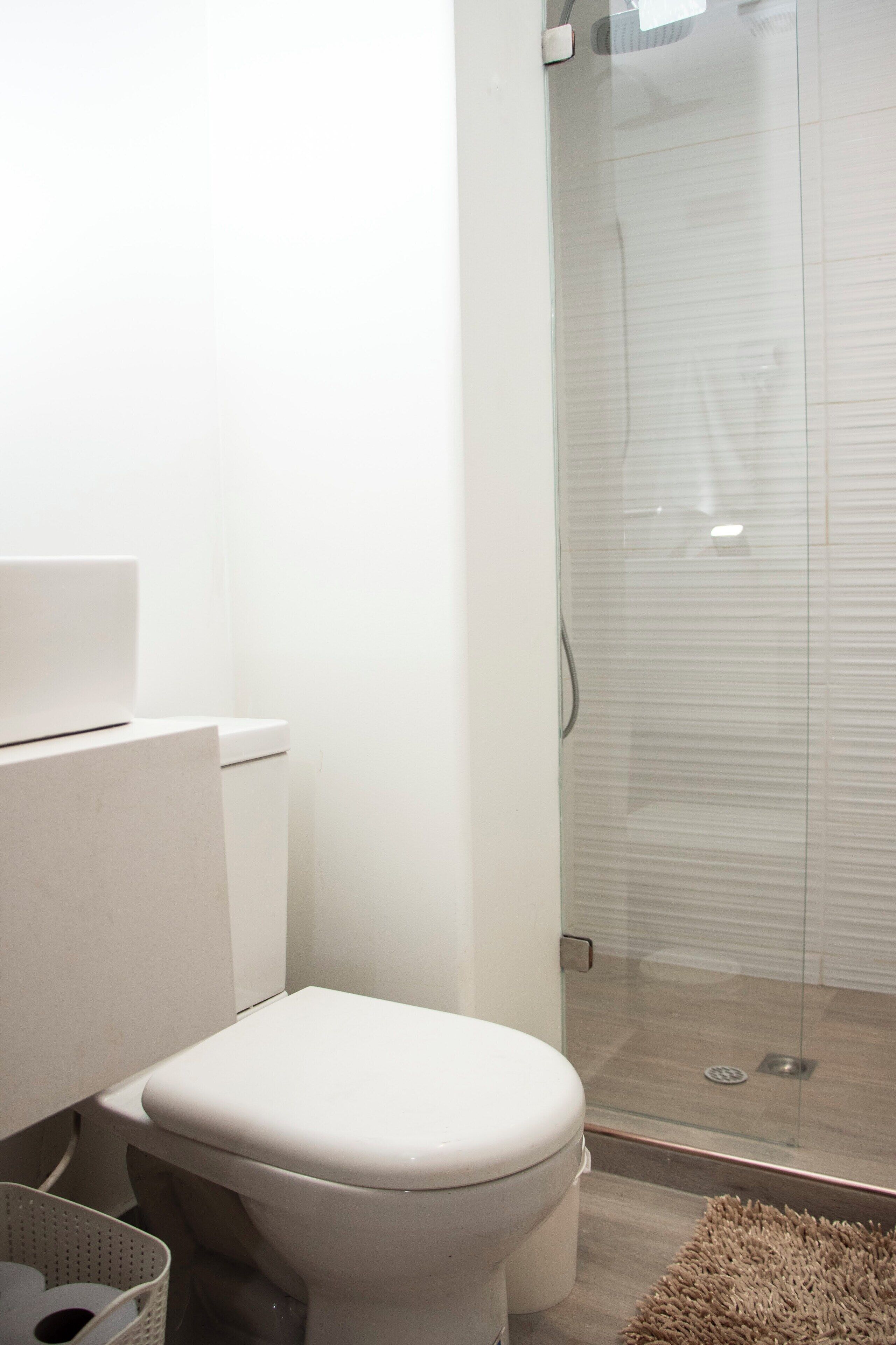 A modern bathroom with a toilet, a glass shower enclosure, and a white sink.