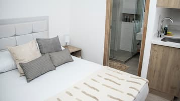 Ein Schlafzimmer mit Bett, Kissen, einem Nachttisch, einer Lampe, einem Badezimmer mit Glastür und einem Holzschrank.