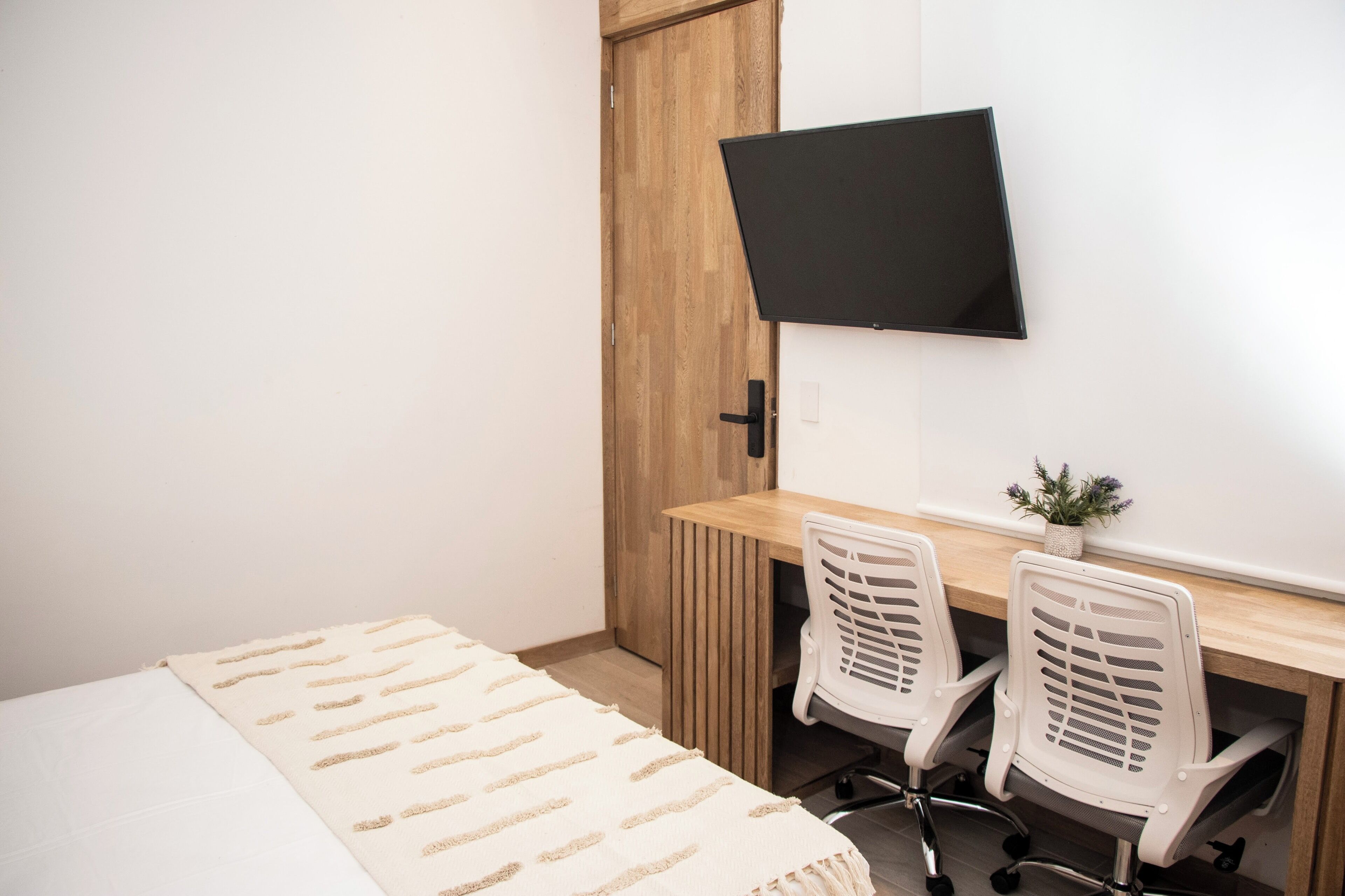 Une chambre à coucher comprenant un lit, un bureau, deux chaises, un téléviseur et une armoire en bois.