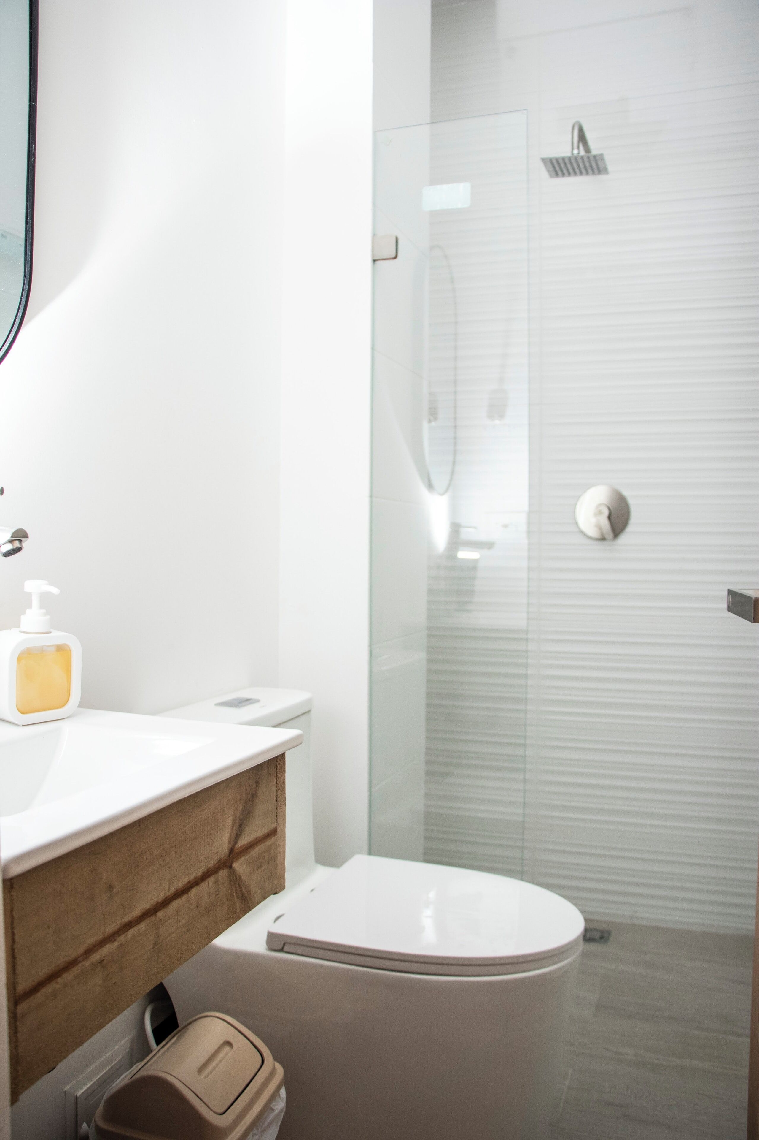 Een moderne badkamer met een douchecabine van glas, een wit toilet en een wastafel met zeepdispenser.