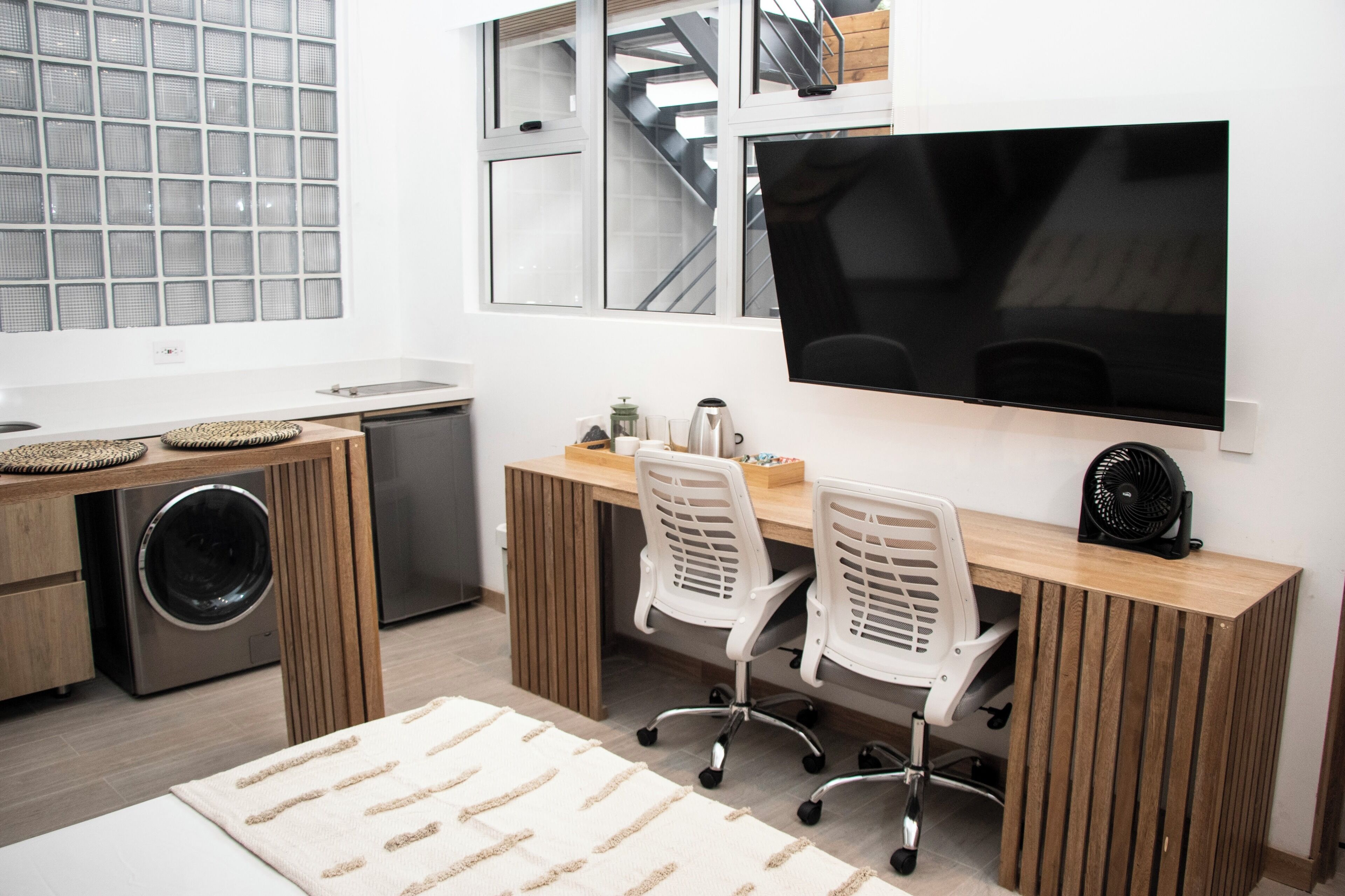 Une cuisine moderne équipée d’un lave-linge intégré, d’un grand téléviseur à écran plat et d’un bureau en bois avec deux chaises de bureau.