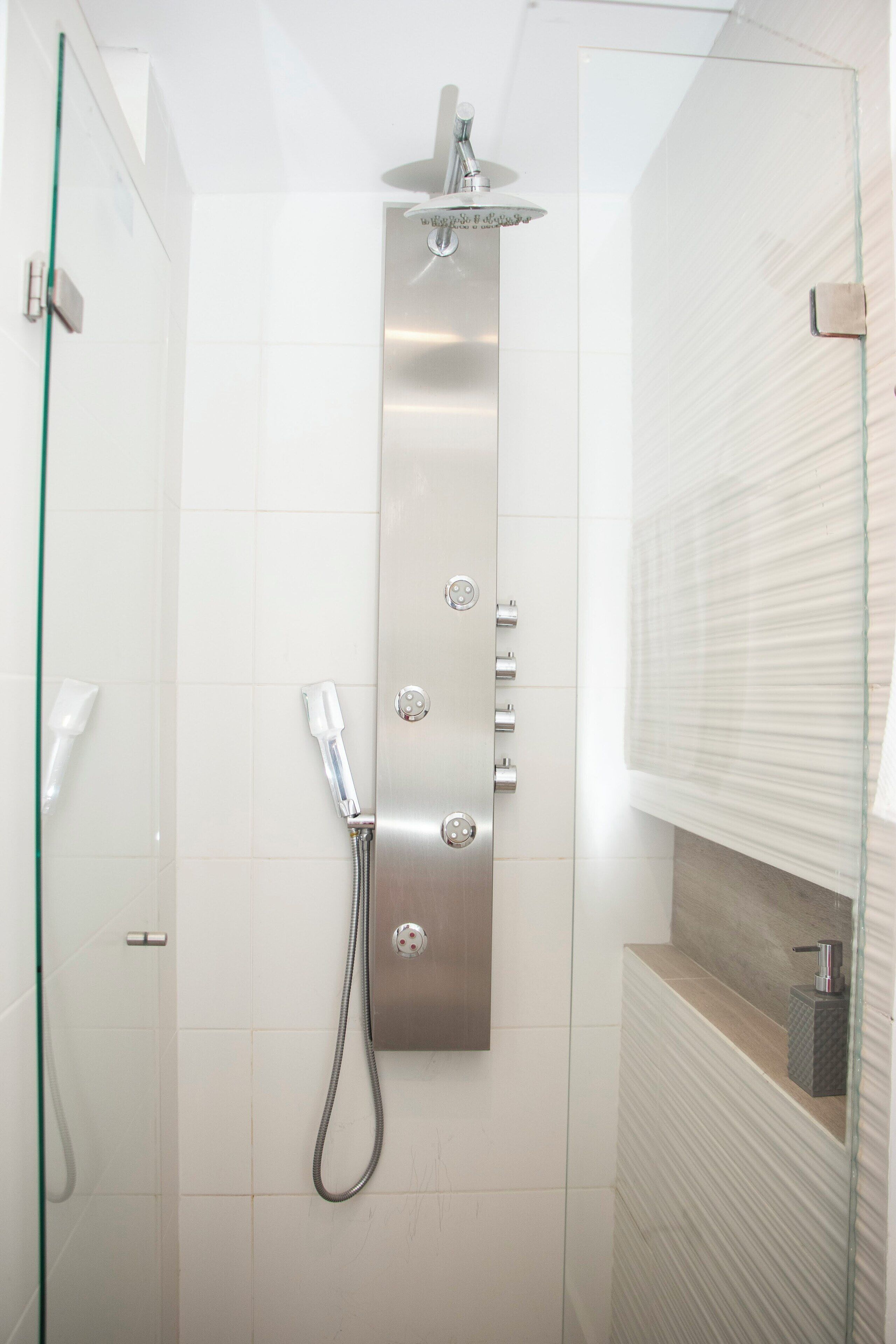 Une douche moderne dotée d’un pare-douche en verre, d’un pommeau de douche à main et d’un panneau de commande fixé au mur.