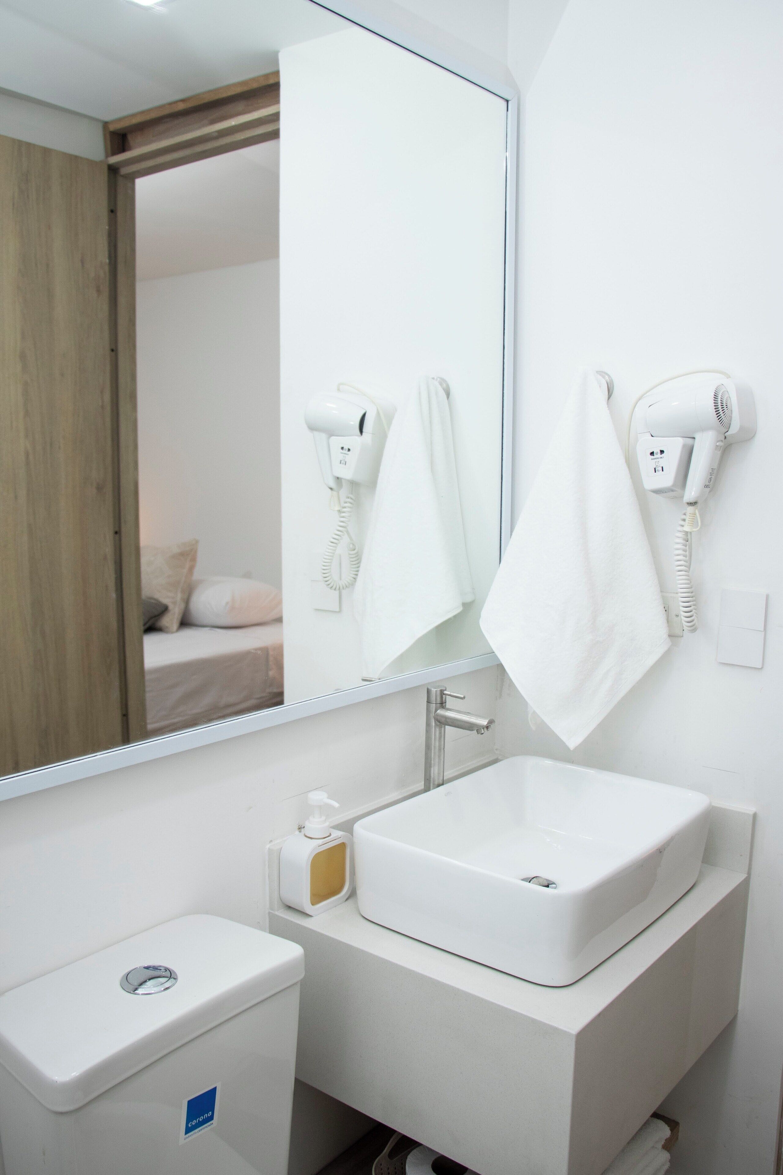 Un baño moderno con un lavamanos blanco, un inodoro y un secador de pelo montado en la pared.
