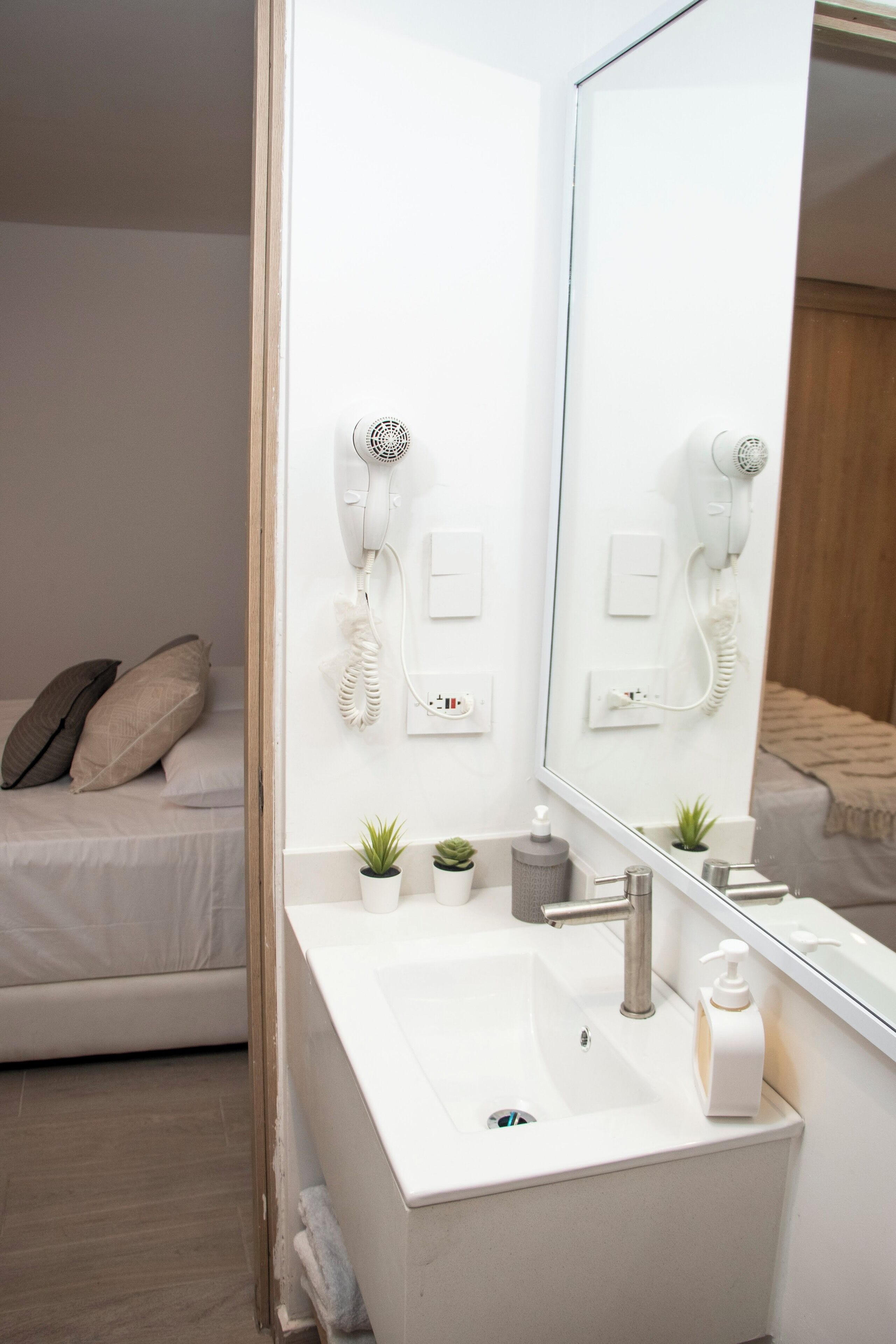 Un baño moderno con un lavabo blanco, un espejo grande y un secador de pelo montado en la pared.