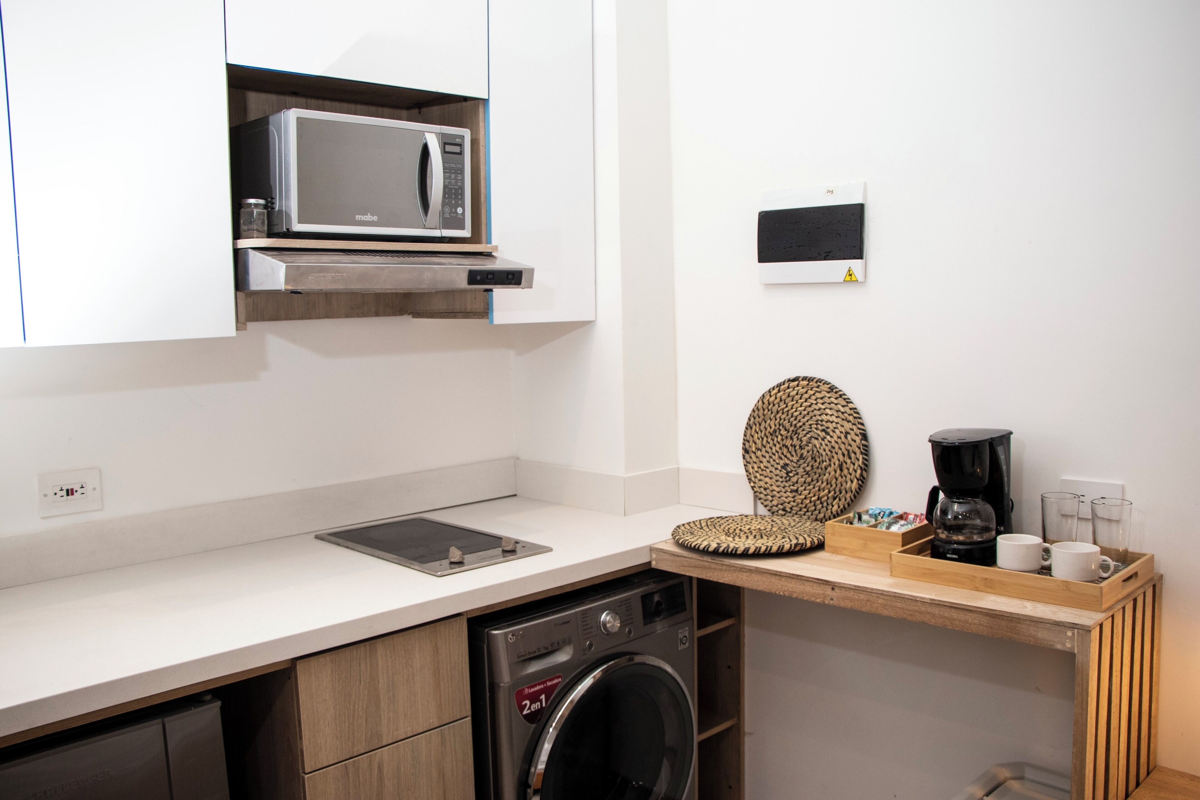 Une cuisine compacte équipée d’un four à micro-ondes, d’une machine à café et d’un lave-linge.