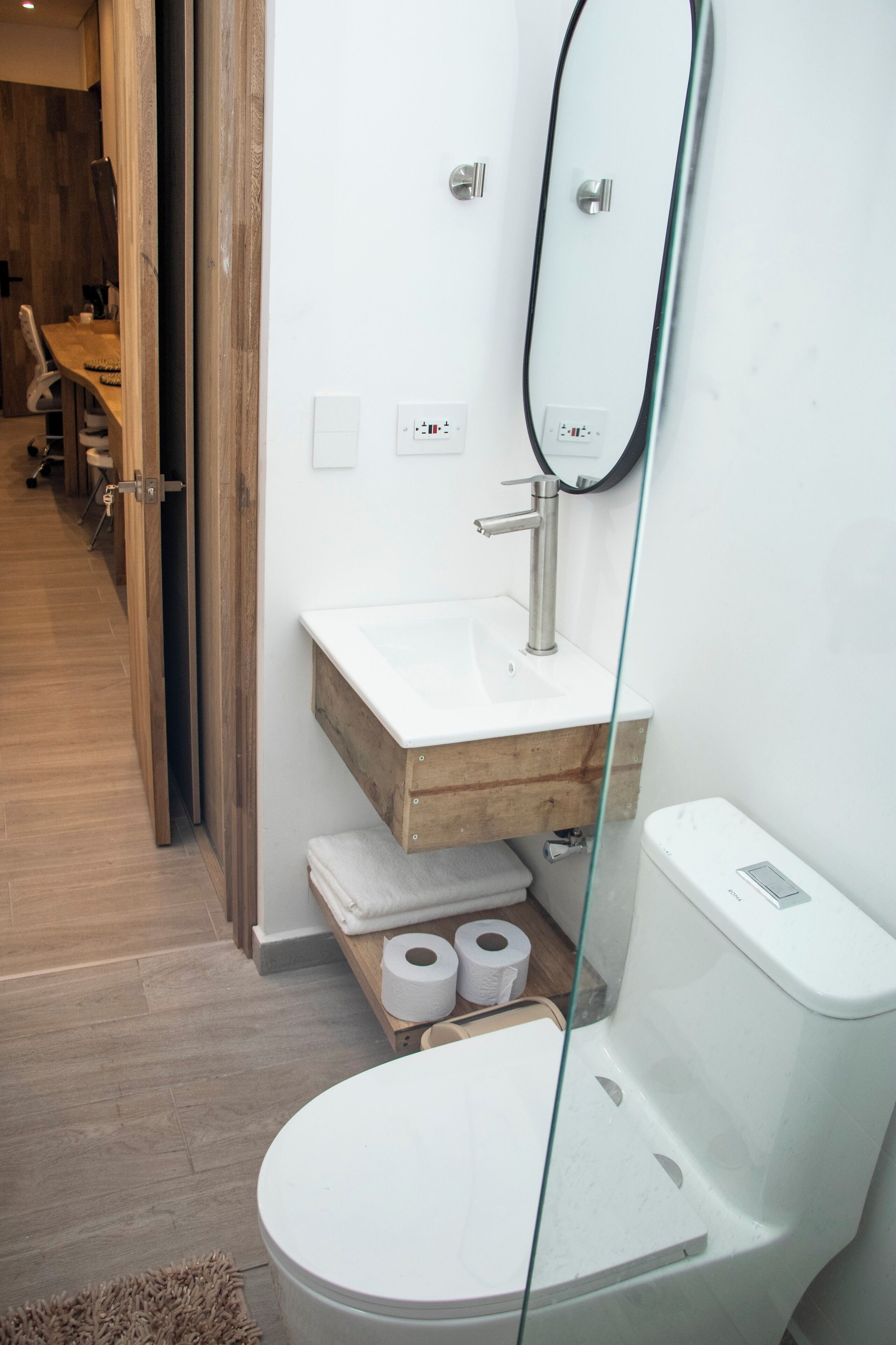 Een moderne badkamer met een wit toilet, een houten wastafelmeubel en een douchecabine van glas.