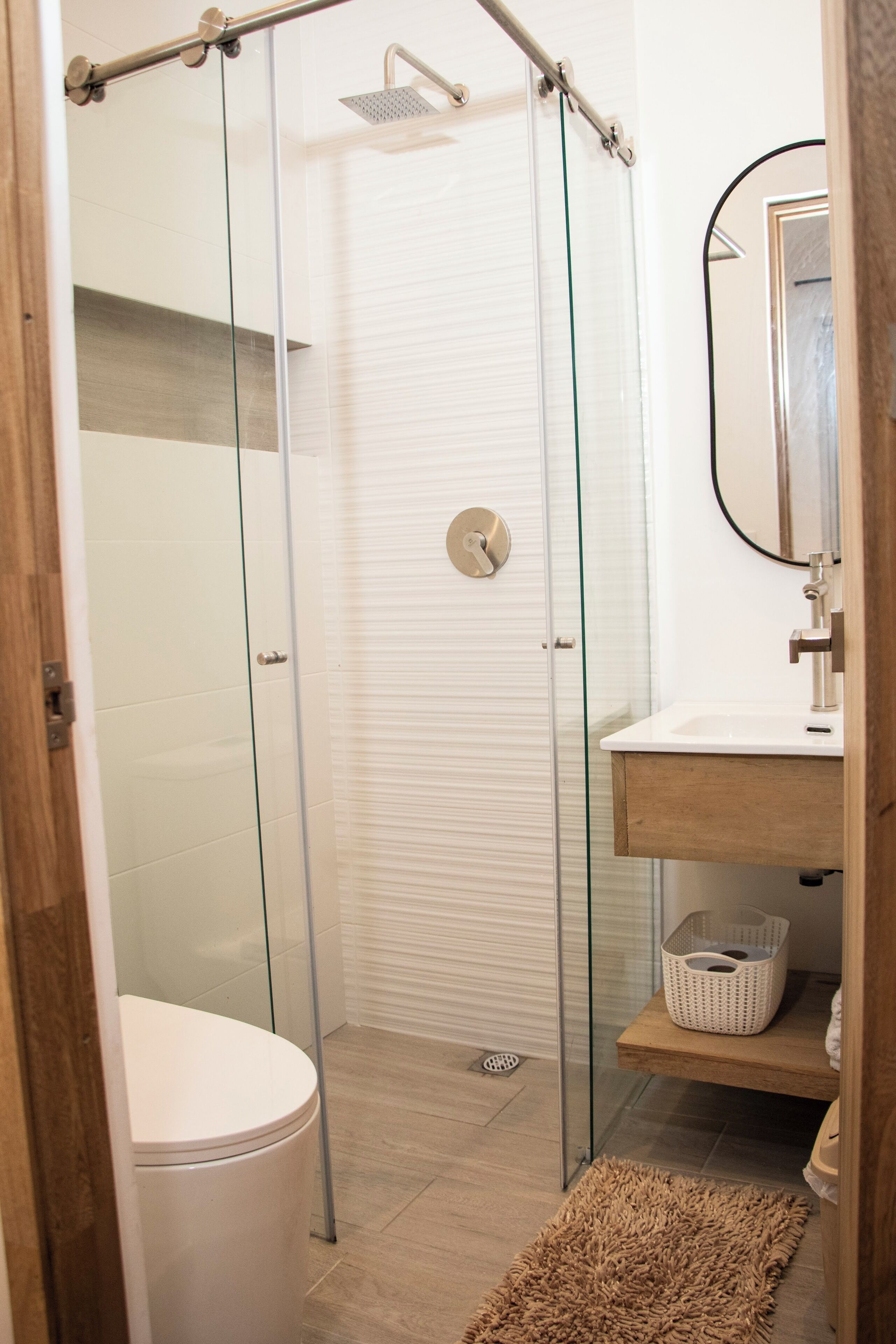 Une salle de bain moderne avec une douche à parois de verre, des toilettes blanches, un meuble-lavabo en bois et un miroir.