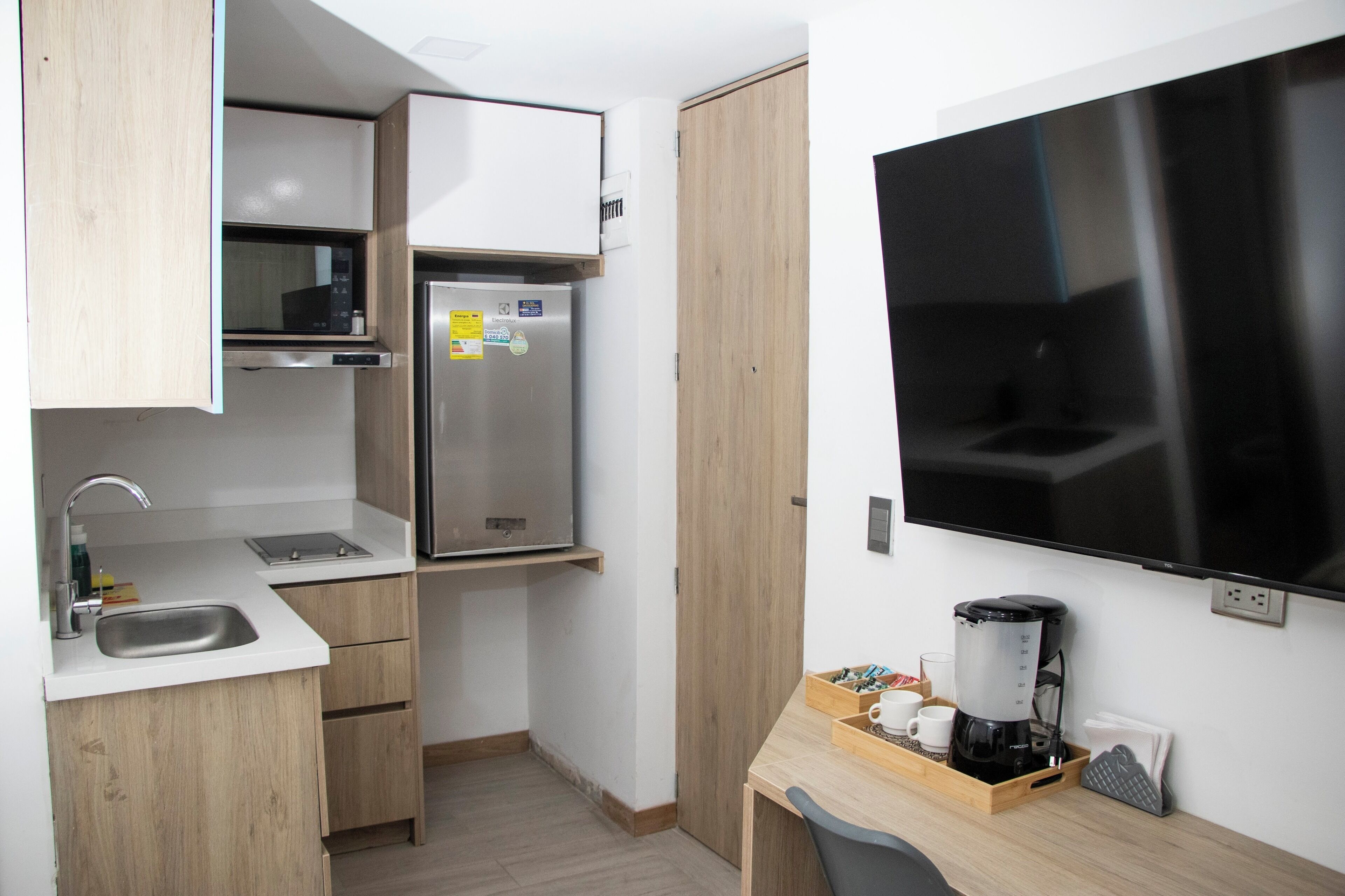 Una cocina compacta con microondas, refrigerador, lavamanos y cafetera sobre una encimera de madera.